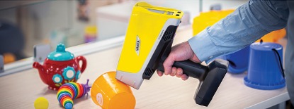 A hand holding a Vanta Max 55 kV analyzer on a plastic child’s cup testing it for RoHS compliance.