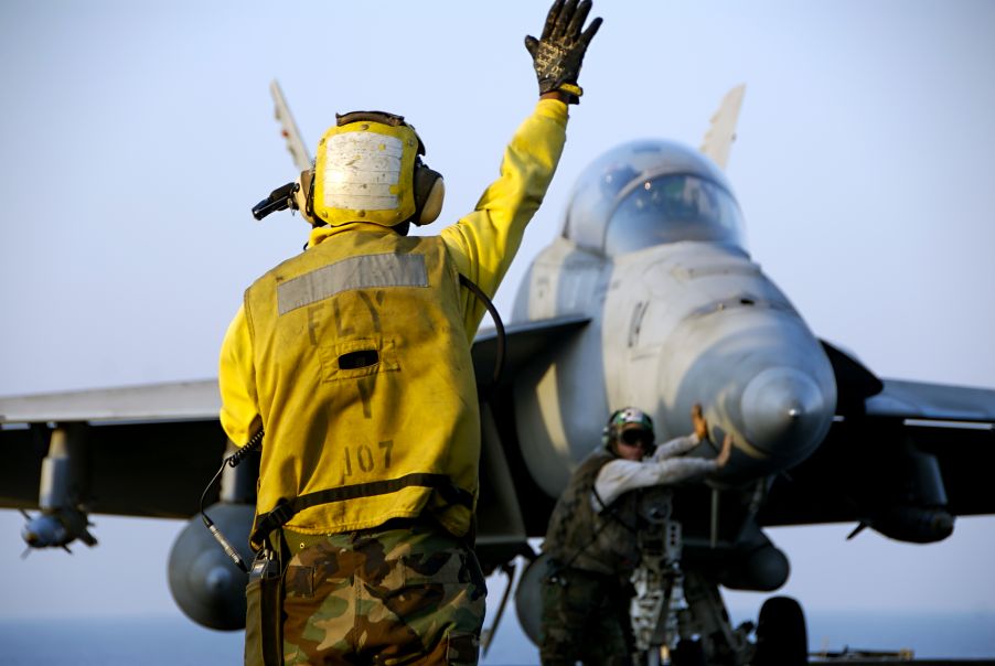 Controllore di aerei dirige un aereo F-18 Hornet fighter sul ponte di una portaerei