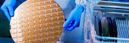 Semiconductor wafer held by a technician in sterile overalls and gloves in a manufacturing facility