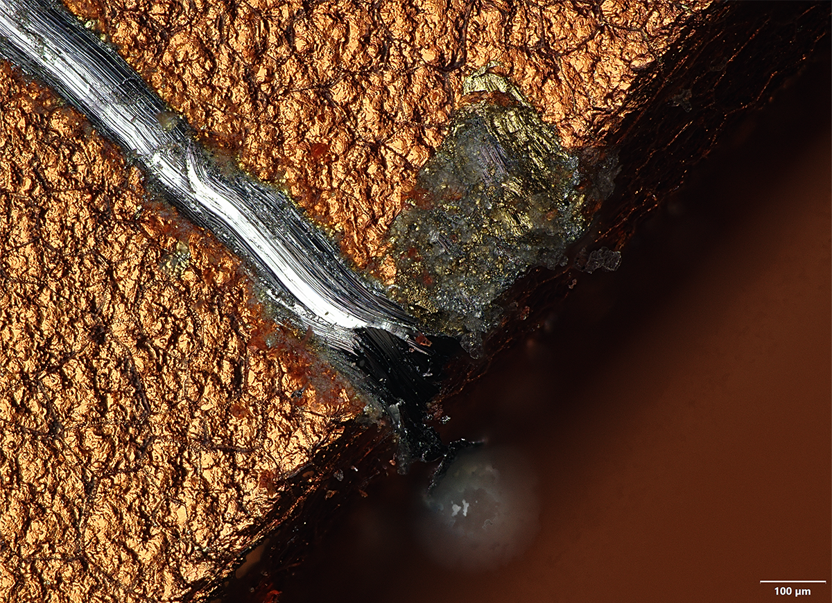 Under a Mohs level-4 pick, roughly the hardness of a coin, the anodized coating chips away at the sharp edge of the camera plateau to reveal bare aluminum. Imaged at 20X in MIX mode.